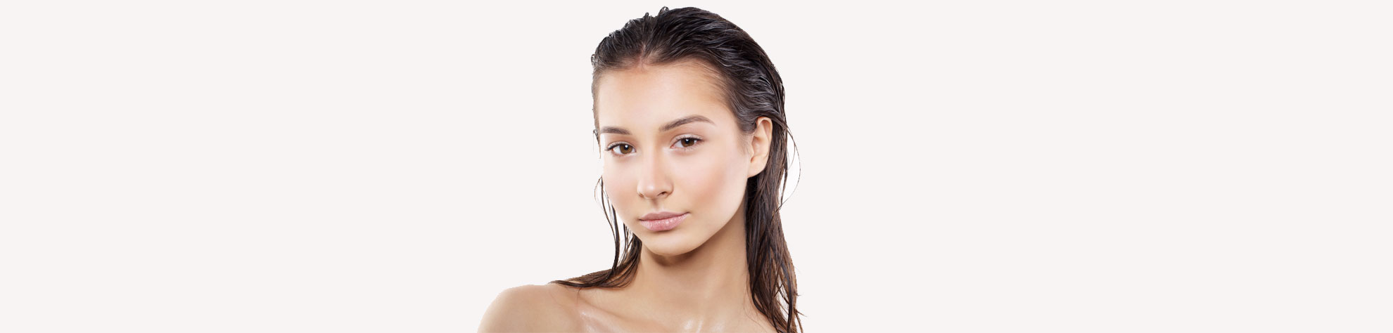 A young woman with wet, slicked-back hair and natural makeup looks confidently at the camera against a plain, light background. Her shoulders are bare, highlighting her clear, glowing skin.
