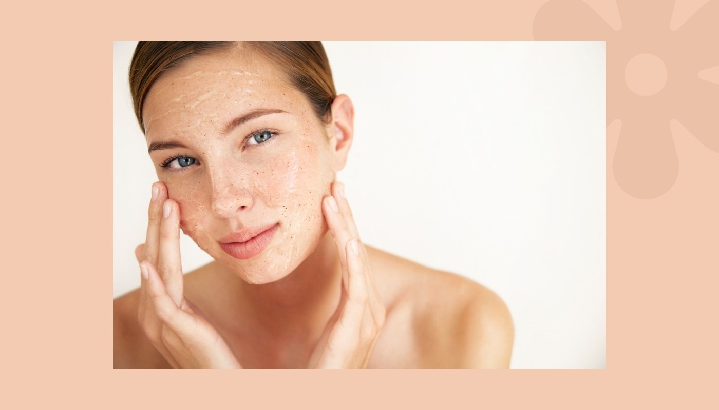 Woman applying facial scrub as part of her essential skin care routine against a neutral background.