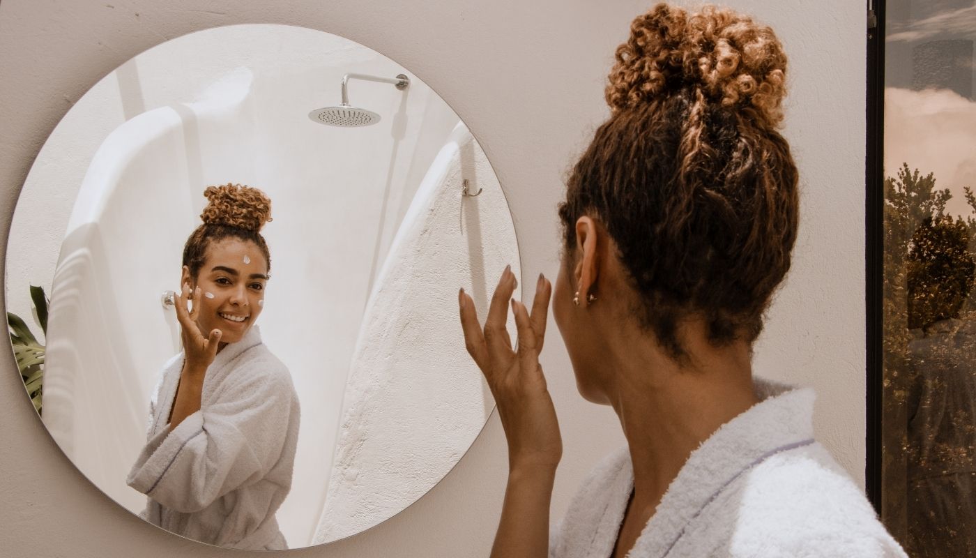 Woman in a robe applies Obagi Retinol for nighttime renewal while looking in a bathroom mirror.