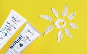 Two Obagi mineral sunscreen tubes and a sun shape made of lotion on a bright yellow background.